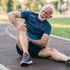 A senior man on a running track, holding his painful knee.
