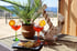 Zwei orangefarbene Cocktails und ein Teller mit Snacks auf einem Tisch, mit Ankerdeko und Palme im Hintergrund.