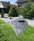 Garten mit Zierkies, grünen Sträuchern und einem modernen Steinelement mit Schale.