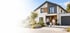 Modernes zweistöckiges weißes Einfamilienhaus mit Flachdach, großen Glasfronten, Garage und gepflegtem Garten bei Dämmerung.