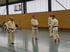 Vier Männer in weißen Karate-Anzügen und Gürteln stehen in einer Sporthalle.