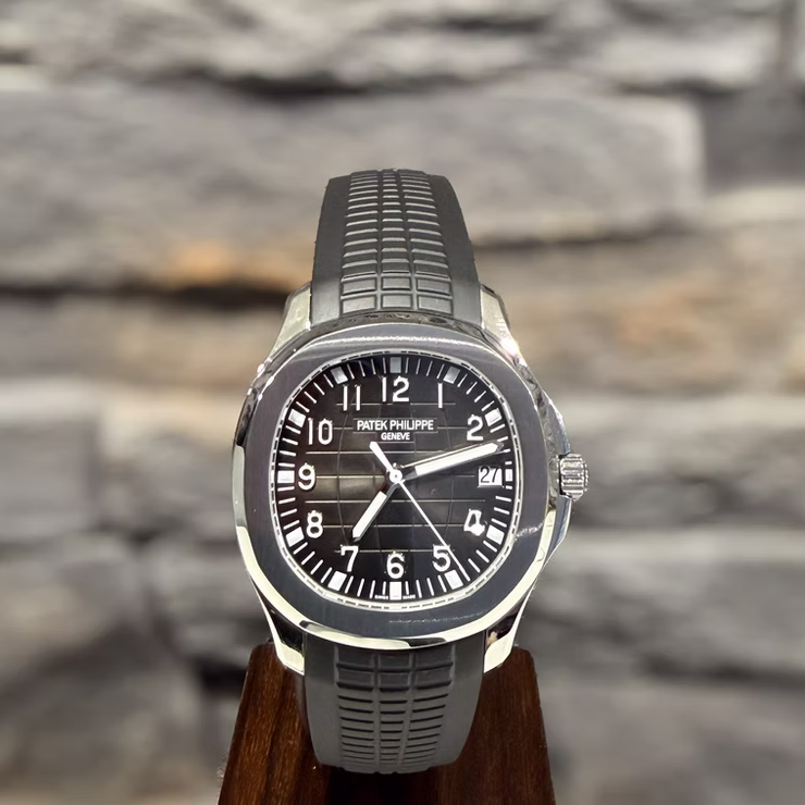 Patek Philippe Aquanaut Uhr mit grauem Kautschukarmband, schwarzem Zifferblatt und Datumsanzeige auf einem Holzständer.