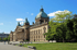 Historisches Reichsgerichtsgebäude in Leipzig mit Kuppel, Säulen und hellgrünen Bäumen unter blauem Himmel.