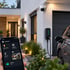 Smart Home App steuert Wallbox am E-Auto, Überwachungskamera und Beleuchtung an einem modernen Wohnhaus.