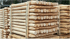 Gestapelte, hellbraune Rundholzpfähle mit zugespitzten Enden auf einer Holzpalette im Freien.