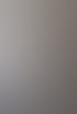 Ein junger Mann mit Brille und Zopf lächelt, trägt ein weißes Hemd und sitzt vor einer grauen Wand.