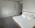 Schlafzimmer mit weißem Bett, grauer Teppich, Einbauschränke und offene Tür.