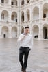 Lächelnder Mann mit weißem Hemd und karierter Hose trägt einen blauen Blazer über der Schulter.