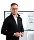 Ein Mann mit Brille und schwarzer Fleecejacke steht vor einem Whiteboard mit den Notizen Marketing, Sales und Fulfillment.