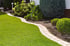 Geschwungener Gartenweg aus Pflastersteinen neben grünem Rasen und Blumenbeeten mit Hortensien und Büschen.