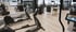 Modernes Fitnessstudio mit schwarzen Trainingsgeräten und hellem Holzboden, ein Spiegel reflektiert den Raum.