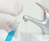 Gloved hands collecting a water sample from a running kitchen faucet into a test tube during a Michigan well water test