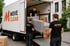 Drei Umzugshelfer in schwarzen MOVE CLEAR T-Shirts laden ein Sofa und Kartons in einen weißen Umzugswagen.