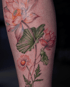 Filigranes Tattoo einer Lotusblüte, Knospe und Gänseblümchen in sanften Rosa- und Grüntönen auf menschlicher Haut.