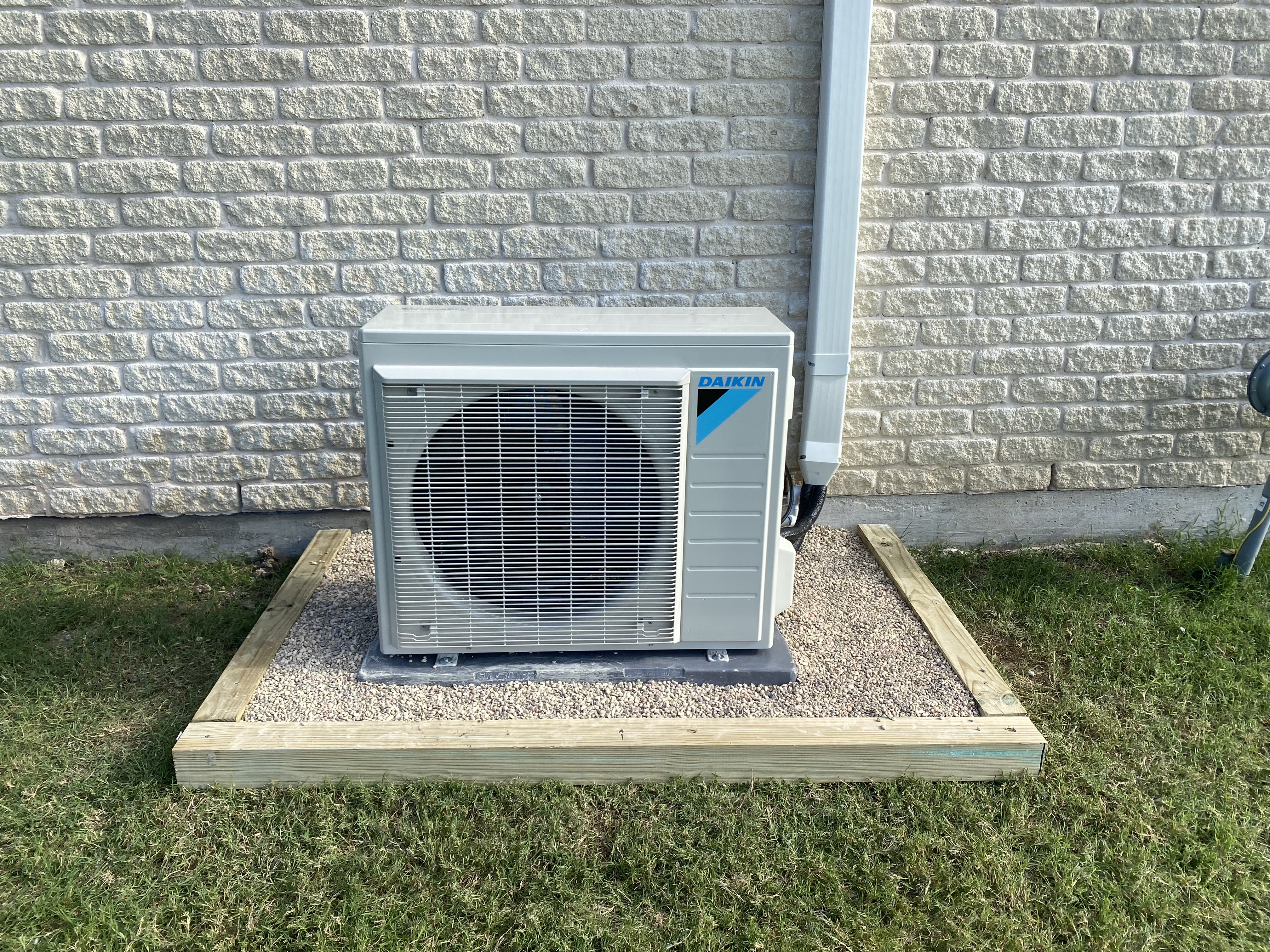 Daikin ductless mini split condenser on a gravel pad beside a brick wall
