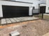 Modernes weißes Haus mit schwarzem Garagentor, gepflasterter Einfahrt und einem schwarzen Metallzaun auf einer Baustelle.