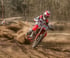 Motocrossfahrer in roter Schutzkleidung auf einem roten Motorrad mit der Nummer 550, wirbelt Staub auf einer Rennstrecke auf.