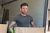 Ein Mann steht vor einem geöffneten Umzugswagen mit Möbeln, darunter ein graues Sofa und ein Kühlschrank.