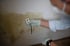 Eine Person misst mit einem Feuchtigkeitsmesser eine große, dunkle Schimmelfläche an einer hellen Wand.