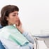 Woman in dental chair, holding her jaw in pain.