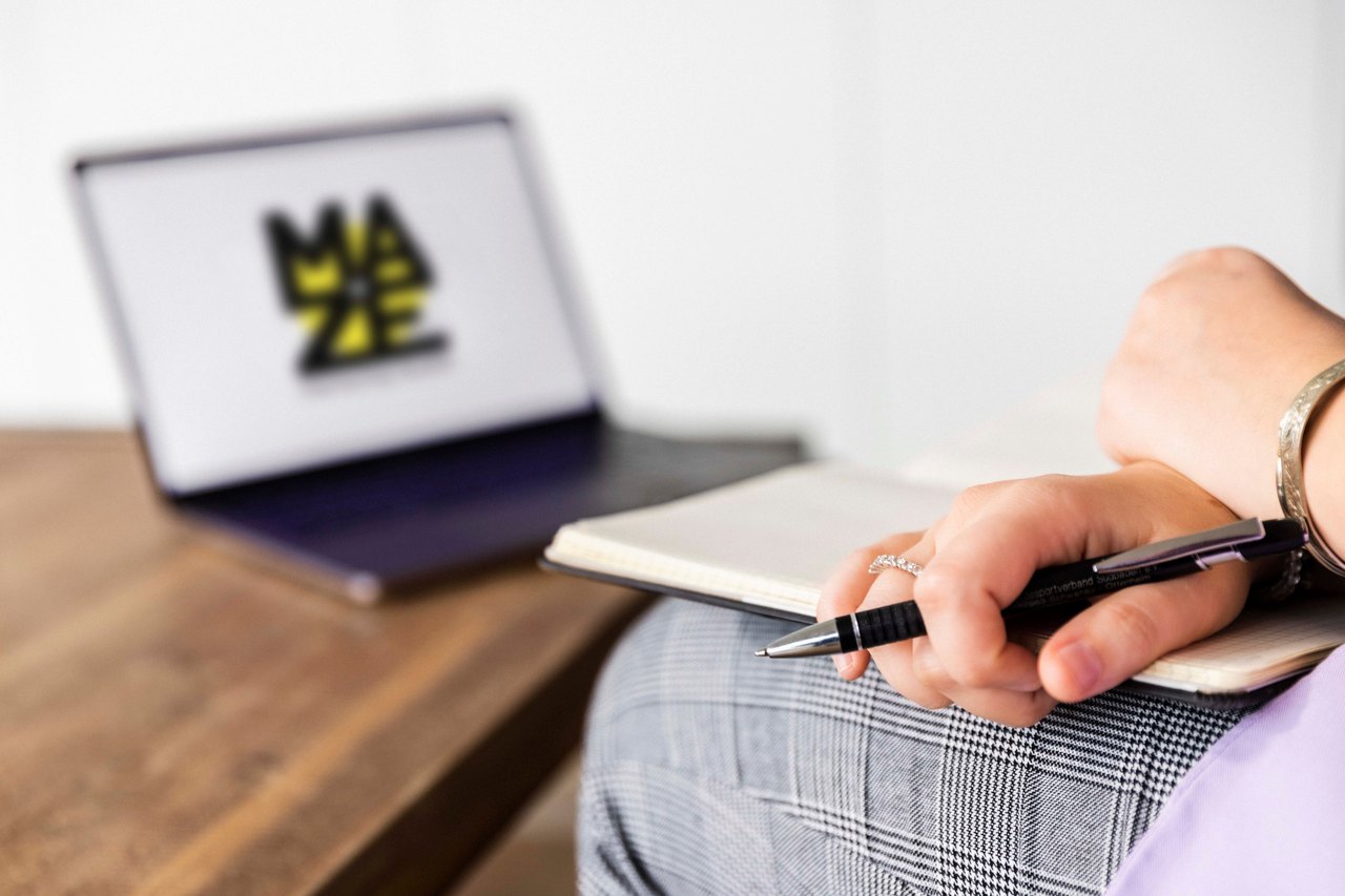 Laptop mit der MAZE-Website, davor ein Notizbuch