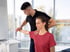 A male physical therapist assists a woman with arm and shoulder stretching exercises in a bright clinic setting.