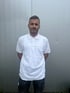 Ein Mann mit kurzem, grauem Haar und Bart in einem weißen T-Shirt blickt nach vorne.