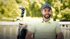 Mann in grünem T-Shirt schlägt einen Golfball auf einem grünen Golfplatz mit Palmen.