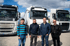 Vier Männer stehen vor drei weißen Volvo-Lastwagen unter bewölktem Himmel.