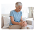 Woman sits on a couch, clutching her right knee joint in pain.
