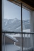 Blick aus einem Fenster mit vereistem Rahmen auf verschneite Berge, Wälder und Holzhäuser bei Tageslicht.
