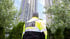 Sicherheitsbeamter mit gelber Jacke und der Aufschrift "SECURITY" blickt auf hohes Gebäude.