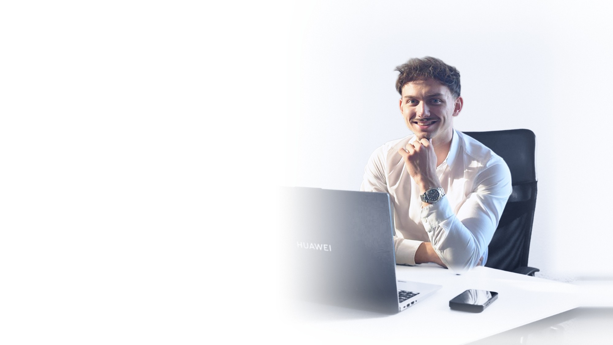 Erman Sapmaz sitzt lächelnd am Schreibtisch vor seinem Laptop