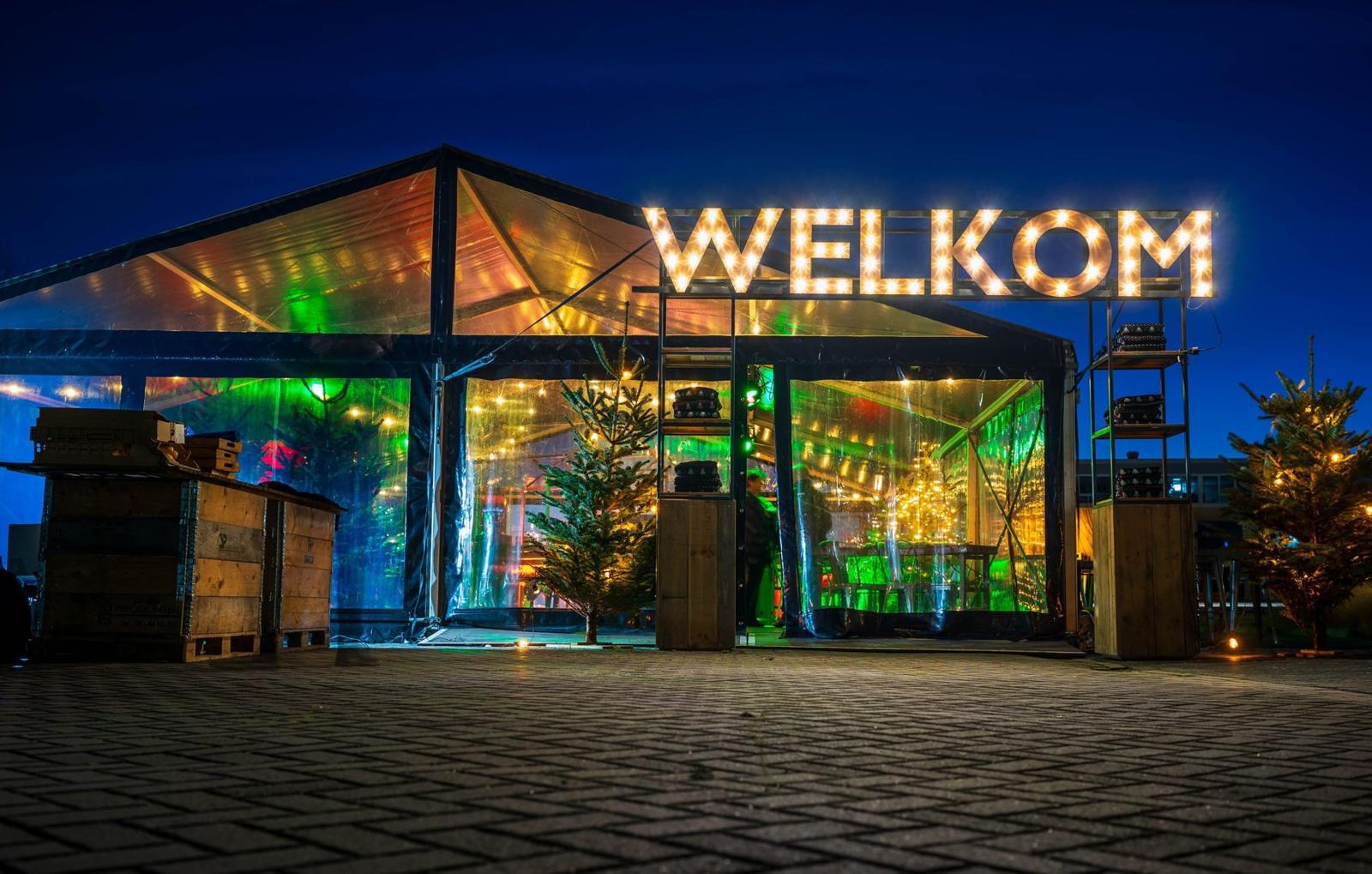 Verlichte feesttent met WELKOM in lichtletters, opgebouwd voor een evenement