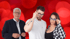 Drei Personen, zwei Frauen und ein Mann, halten sich Brillen ins Gesicht, vor einem roten Bokeh-Hintergrund.