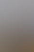 Lächelnde blonde Frau mit Brille und grauem Oberteil sitzt am Tisch im Büro. Im Hintergrund hängt ein Kaffeeschild.