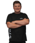 Lächelnder junger Mann mit verschränkten Armen und schwarzem T-Shirt mit Aufschrift "L. THOMAS MECHANIKER".