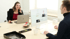 Eine Frau telefoniert am Laptop, ein Mann arbeitet am Desktop-Computer im Büro.