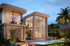 Modern two-story villa with large windows, an outdoor pool, patio loungers, and a fire pit, surrounded by lush green landscaping.
