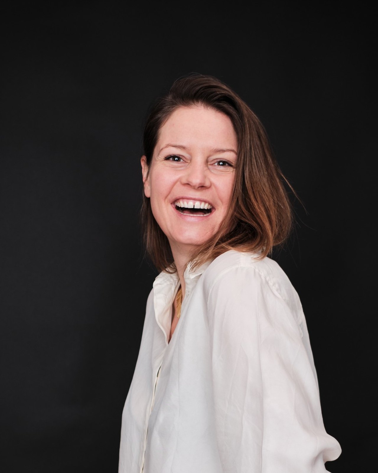 Katharina Baier, Coach und Trainerin, lachend in weißer Bluse vor schwarzem Hintergrund