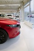 Rotes Auto in einem Ausstellungsraum mit weiteren Autos und großen Fenstern.