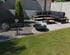 Moderne Terrasse mit Pflastersteinen, Lounge-Möbeln, Feuerschale und Schild der Pflastermanufaktur neben einer Rasenfläche.