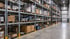 Hohe Industrieregale in einem Logistikzentrum sind mit zahlreichen Paketen und Waren auf Holzpaletten gefüllt.