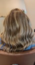 Rückansicht von welligem, schulterlangem Haar mit hellbraunen und blonden Highlights in einem Friseursalon.
