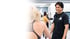 Ein lächelnder Fitnesstrainer im schwarzen T-Shirt steht einer Sportlerin in einem hellen Boxclub gegenüber.