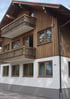 Mehrstöckiges Haus mit Holzfassade, zwei Holzbalkonen und einer weiß verputzten unteren Etage.