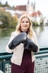 Petra Gruber in Steyr in beiger Jacke und bordeauxroter Hose hält schwarze Boxhandschuhe mit der Aufschrift „BOXEN“, im Hintergrund Steyr.