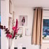 Weiße Wand mit gerahmten Bildern, darunter ein Porträt einer Frau, und ein Blumenstrauß mit rosa Rosen.