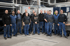 Gruppe von 13 Männern in Arbeitskleidung, die in einer Fabrikhalle lächeln und posieren.