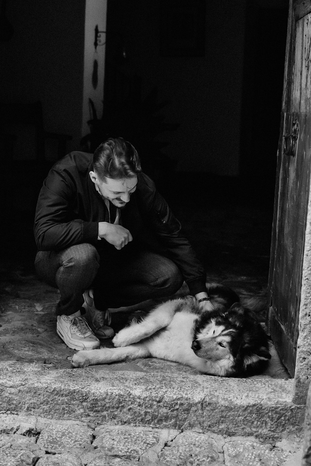 Person hockt bei einem Hund im Türrahmen, Schwarz-Weiß